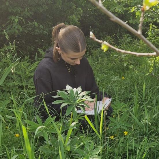 billede af siddende pige der studerer blomster ude i skoven