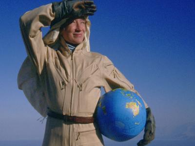 Billede af kvinde omgivet af sand og blå himmel med oppustet plasticjordklode