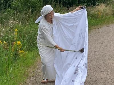 billede af hvidklædt kvinde der står med et lagen ude i naturen