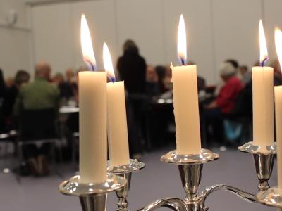 Billedet viser stearinlys foran en forsamling af mennesker, der sidder og lytter.