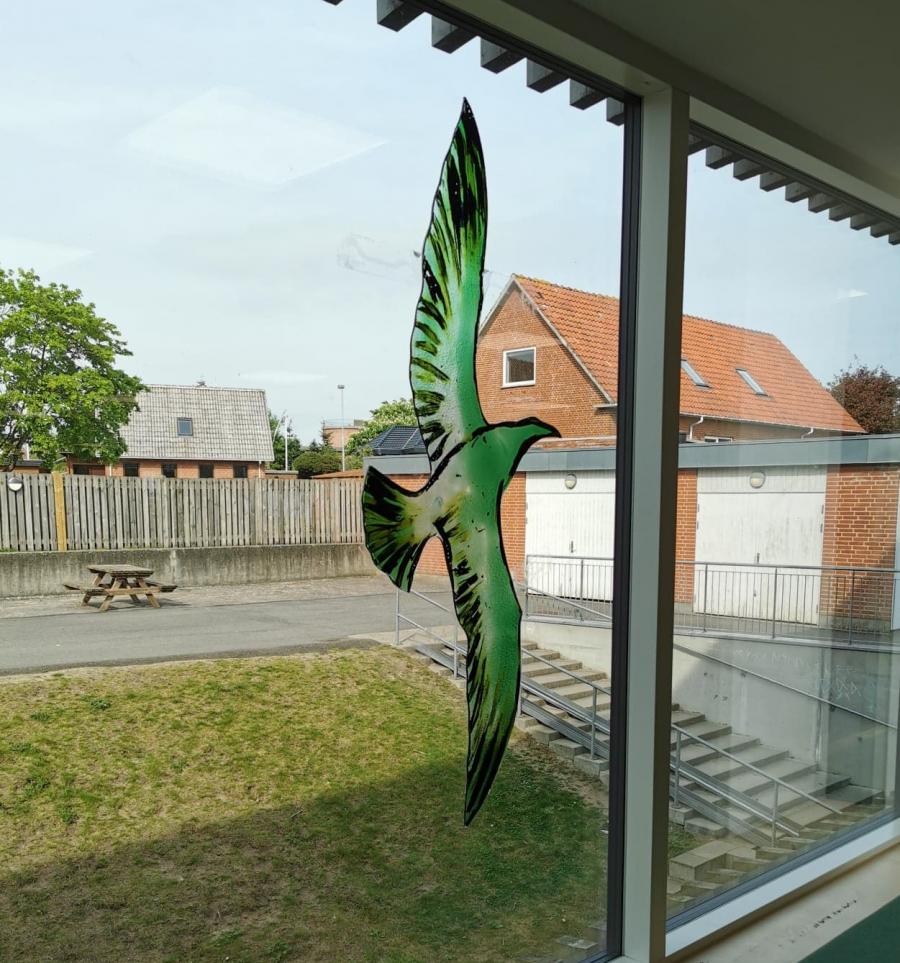 Billedet forestiller en glasfugl lavet af Trondur Patursson som hænger i et vindue på Nørre Snede bibliotek.