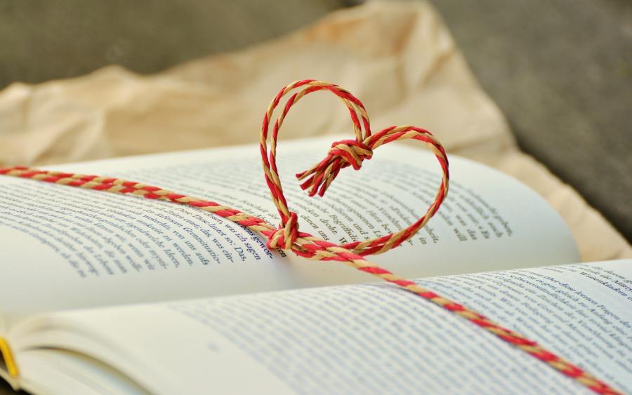 Billedet viser en åben bog med rød/hvid jutesnor rundt om som er foldet op i hjerte.