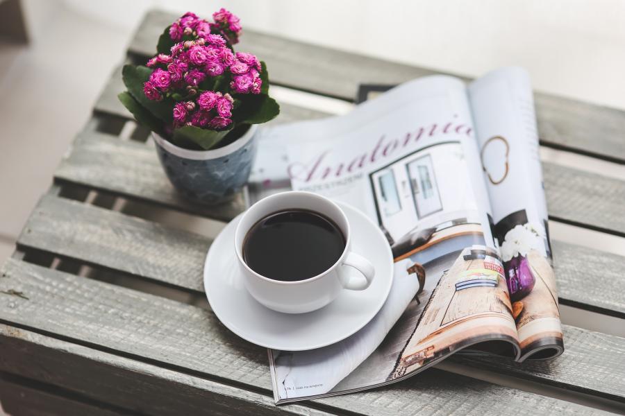 Billedet viser en kop kaffe og to åbne magasiner.