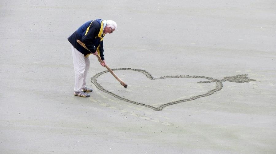 Ældre mand tegner et stort hjerte på stranden.