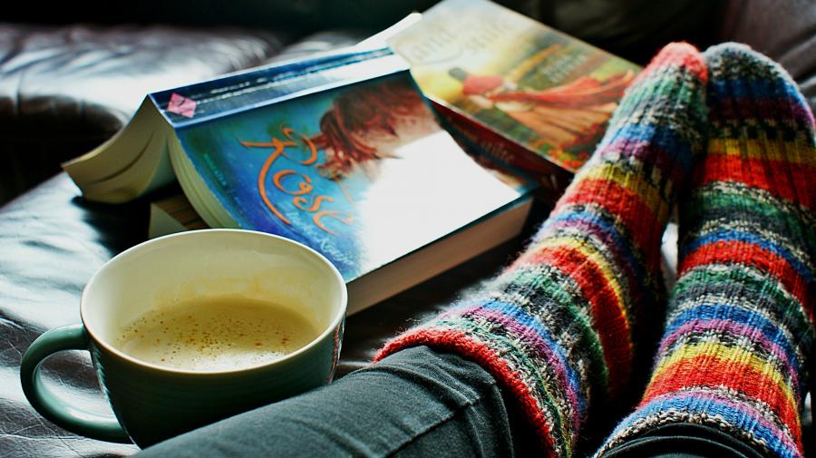 Billedet viser en kop kaffe, to opslåede bøger med coveret opad og et par striksokker.