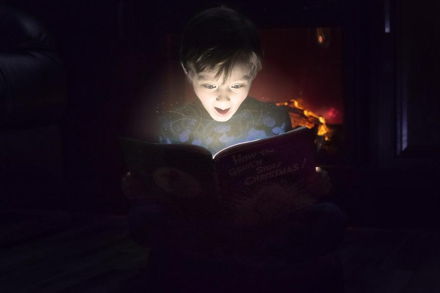 En dreng der sidder i mørke og læse i en bog der er oplyst
